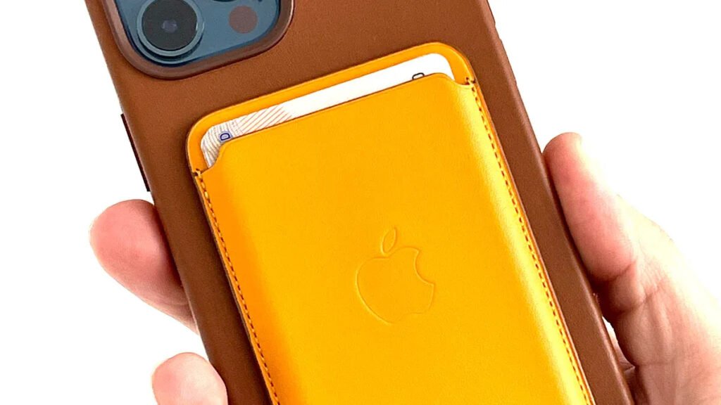 Close - up of a hand holding an iPhone with a brown case and yellow MagSafe magnetic wallet, powered by a magnet ring